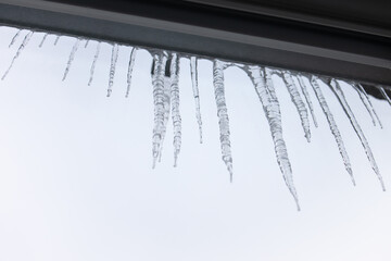 Sharp icicles hanging from eaves of roof. Beautiful transparent icicles slowly gliding of a roof. View from inside