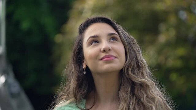 Happy young woman standing outdoors looks up at sky. Grateful 20s adult girls opening eyes smiling