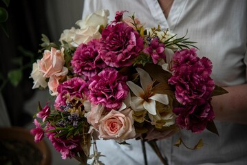 A bouquet of white roses and burgundy carnations in the hand of a woman in a white shirt