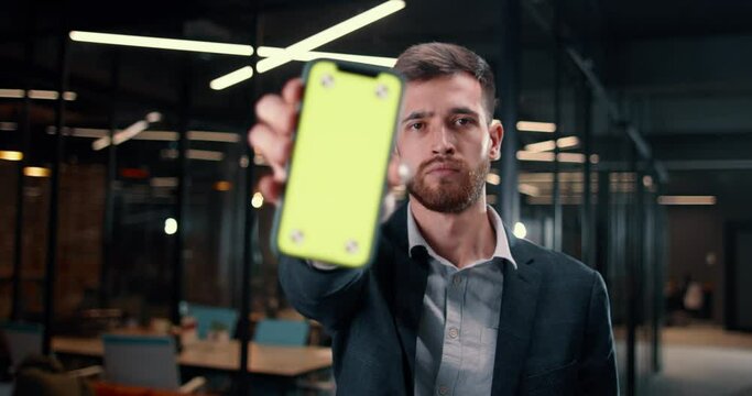 Millennia man looks screen smartphone and stretches hand with smartphone display into camera. Close-up green chroma key on smartphone display insert advertisement for your product service application.
