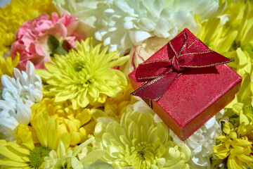 Red jewelry gift box on a bouquet of yellow and white flowers in close-up