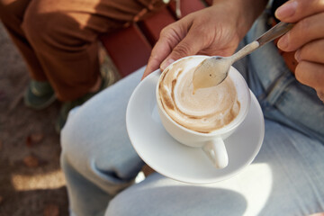 Woman holding a cup of coffee with a spoon outdoors