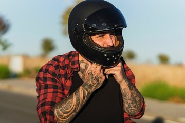 Tattooed man fixing his helmet on a blurred background on a sunny day