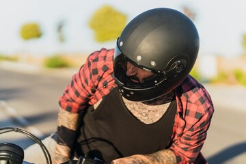 Tattooed man sitting on his bike on a blurred background on a sunny day