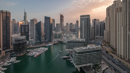 Aerial view to Dubai marina skyscrapers around canal with floating boats day to night timelapse