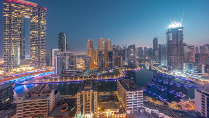 Naklejka premium Dubai Marina with several boats and yachts parked in harbor and skyscrapers around canal aerial night to day timelapse.
