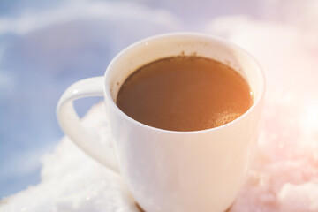 White mug with hot coffee in the snow