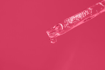 Transparent glass pipette with facial serum, bubbles on magenta background macro. Color of the year 2023. Dropper with drop of essential oil or gel closeup. Cosmetic product with hyaluronic acid.