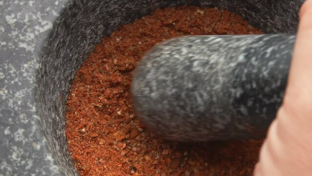 A male hand is grinding a mix of spices, peppers and sea salt with a pestle