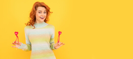 Woman isolated face portrait, banner with copy space. glad redhead girl with red heart sticks on yellow background.