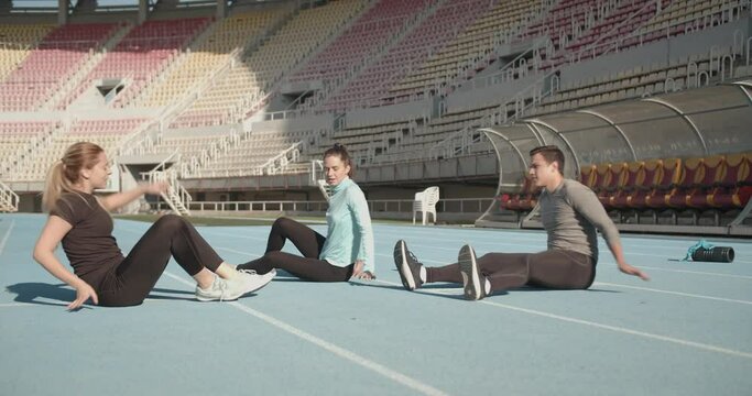 Three young people warming up in the stadium in the morning