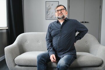 Fototapeta premium Senior man with white hair and beard alone sitting on bed and suffering from low back pain. Old age, health problem and people concept