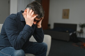 Middle age grey-haired man stressed sitting on sofa at home