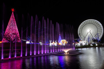Christmas decoration set consisting of a Christmas tree, water with lights and a giant Ferris wheel. Night photo of Christmas lights. - obrazy, fototapety, plakaty