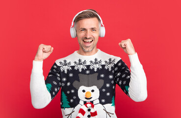 Christmas songs, man with headphone. Portrait of middle aged man in sweater isolated over red background. Concept of holidays, happiness, emotions and Christmas celebration.