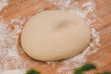 Dough for pizza on a wooden board with white flour and ingredients around ready for preparation, close up