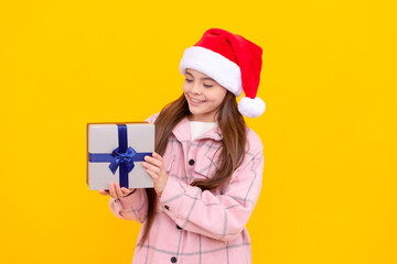 happy kid in santa claus hat. teen girl with gift on yellow background. xmas holiday present.