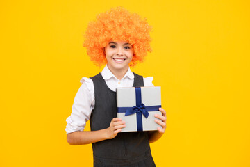 Teenager child in funny wig holding gift box on yellow isolated background. Gift for kids birthday. Christmas or New Year present box. Happy girl face, positive and smiling emotions.