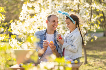father and daughter coloring easter eggs with laptop in the garden