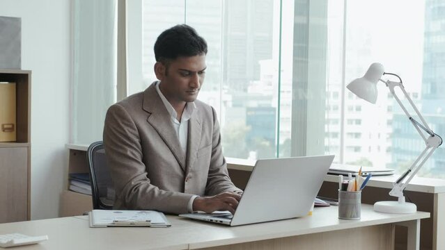 Medium shot of Indian businessman in formal suit working on laptop at office desk