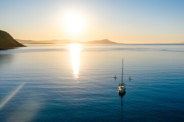 Aerial view of stand up paddlers women and a sailboat at sunset. Tranquil water of Mediterranean...