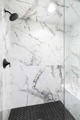 A luxury shower with marble tiled walls, black herringbone tiled flooring, black showerhead, and a...