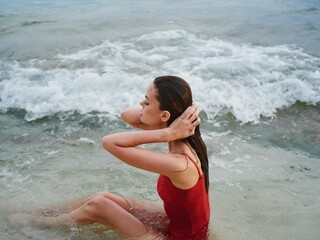 Woman lying on the ocean on the beach in the waves in a red swimsuit, a hotel vacation