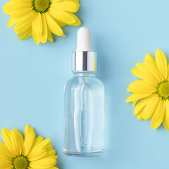 Glass bottle with serum and yellow flowers on a blue background. Cosmetic facial skin care and spa....
