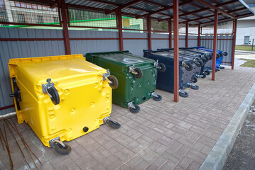New colored plastic garbage bin for sorting various household waste. Colorful plastic bins for different waste under conopy next to new residential building. Place for dumpsters to collect garbage
