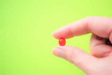 Round red vitamin in human fingers. Vivid green background