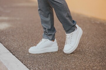Close-up shot of a man wearing white sneakers with gray classic pants