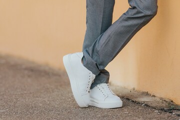 Close-up shot of a man wearing white sneakers with gray classic pants