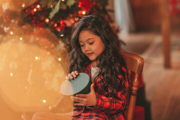 Portrait of candid asian smiling little girl in red plaid pajama sitting with presents at Xmas home
