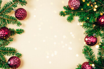 Fir branches and purple Christmas baubles with golden bokeh lights on beige background. Top view, flat lay, copy space