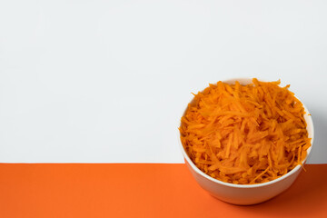 Grated butternut in a white cup on orange background and white