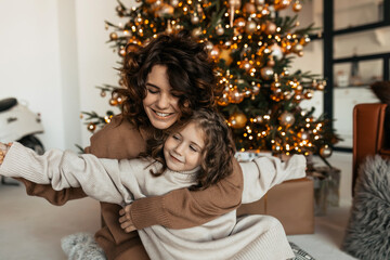 Obraz na płótnie Canvas Cute adorable smiling woman with curly hair wearing sweater holding her little daughter. Family portrait of young woman with daughter