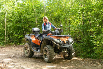 Fototapeta na wymiar Smiling happy woman riding quad bike on a sunny day, against blue sky. Low angle shot. Freedom, happiness, nature concept