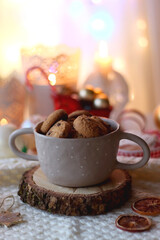 Various Christmas decorations, cup of tea, cookies, lit candles and soft blanket on the table. Colorful Christmas lights in the background. Selective focus.