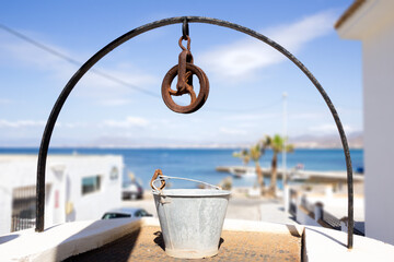 An old well with a bucket and a blurred sea on the background.