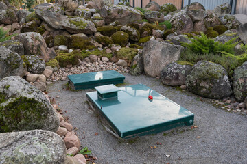 Square green metal cover of an autonomous septic tank with a warning lamp on the backyard among rocks. Sewer system of the house