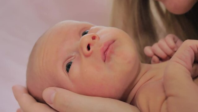 Close-up of face of newborn baby. Caucasian child laying on mothers hand and she kisses him. Slow motion shot