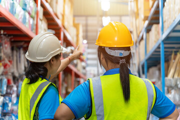 Asian teamwork of Warehouse workers Wearing Hard Hat Holding Digital Tablet checking packages on shelf in a large store. Working in Logistics and Distribution Center. Working Woman Concept.
