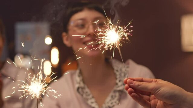 Young happy woman and her cheerful friends holding sparklers while celebrating Christmas together at home