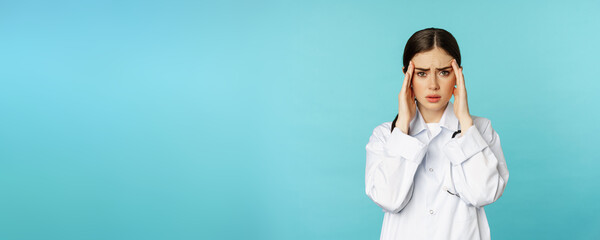 Image of woman doctor, medical personel grimacing from discomfort, having headache, migraine, feeling deezy, standing over torquoise background - obrazy, fototapety, plakaty