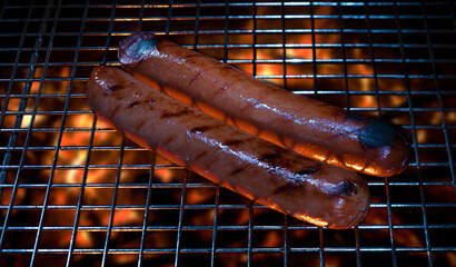 Two plump hot dogs cooking over a BBQ