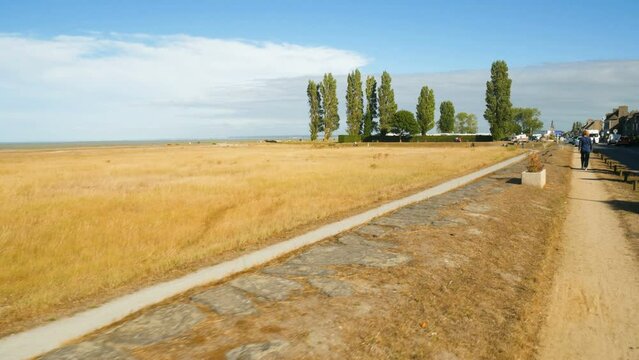 Walking on a dry dirt road, on the colorful flat coastline of Saint Benoit Des Ondes during low tide. The Atlantic ocean is visible in the distance. Blue sky on the background.