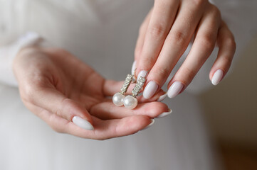 Close-up of an earring with white pearls in the hands of brides.The concept of the morning of the...