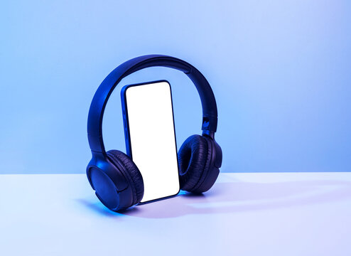 Smartphone with bluetooth headphones with white screen on blue neon background, for mockup and logo.