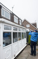A window and gutter cleaner cleaning Dirty clogged white plastic pvc gutters and drain pipes with...
