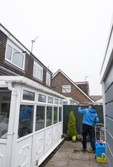 A window and gutter cleaner cleaning Dirty clogged white plastic pvc gutters and drain pipes with...